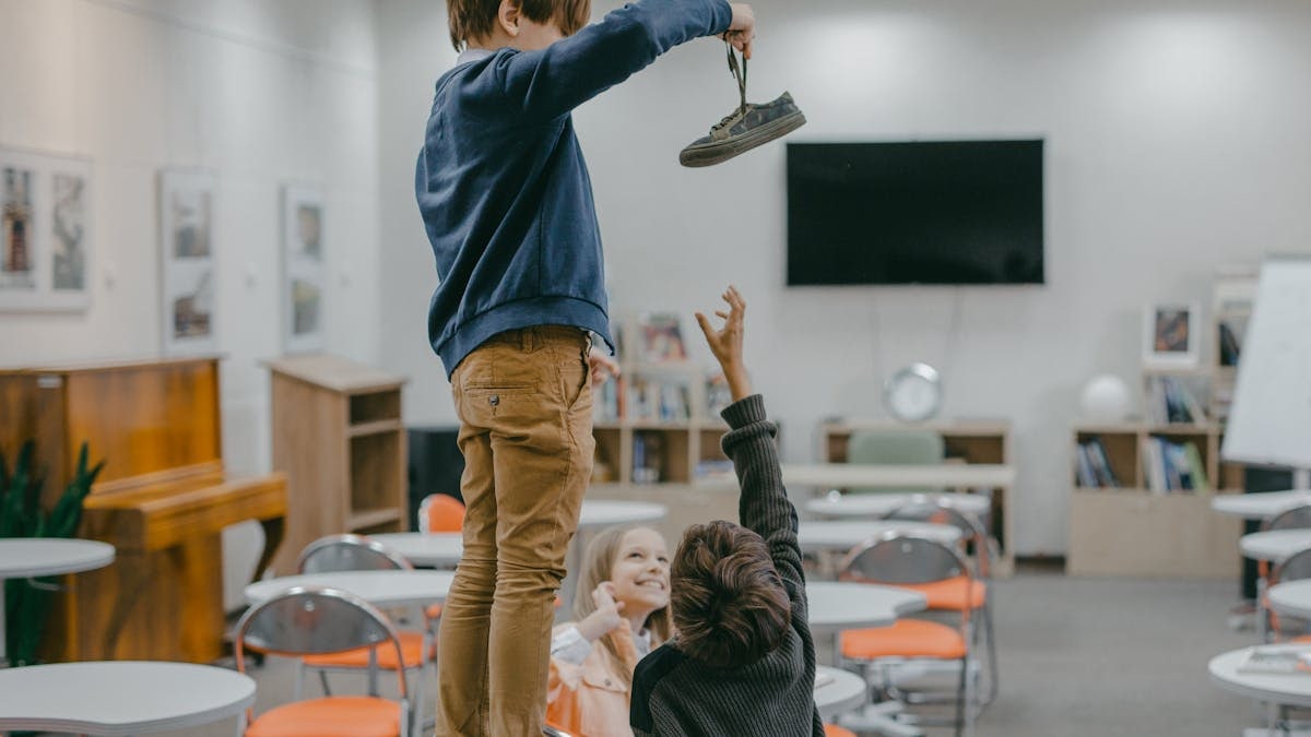 Children interacting in a classroom setting, playfully reaching for an object.