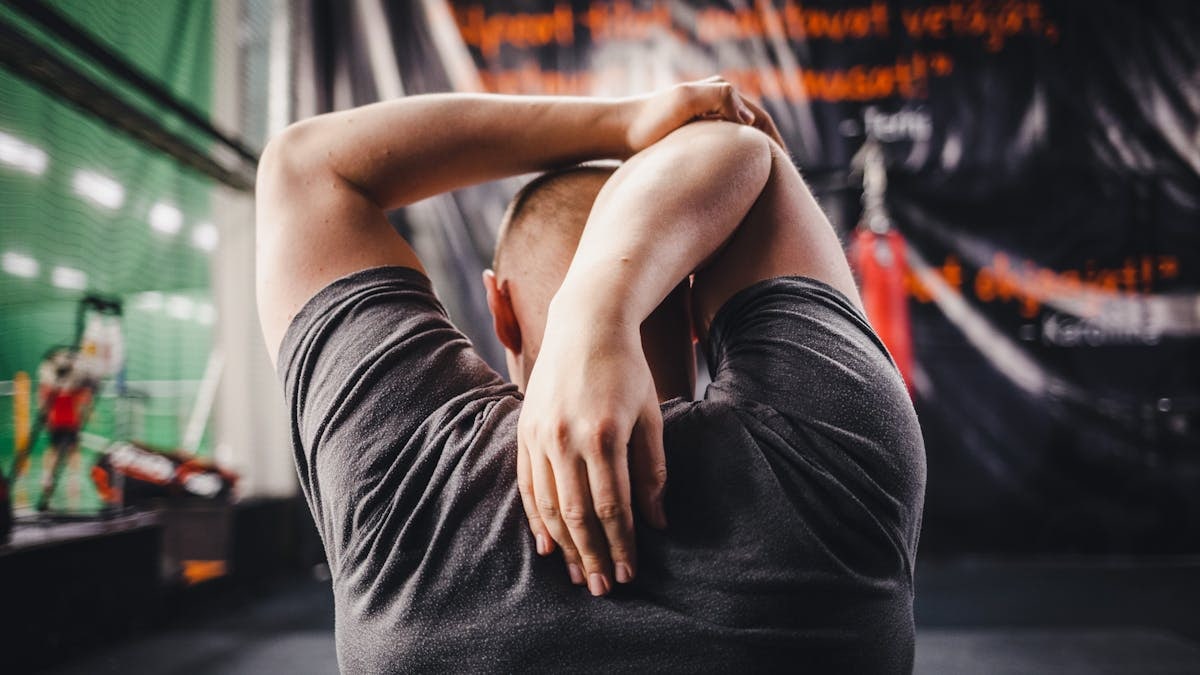 Man stretching arms in a gym, viewed from behind, focusing on fitness and flexibility.